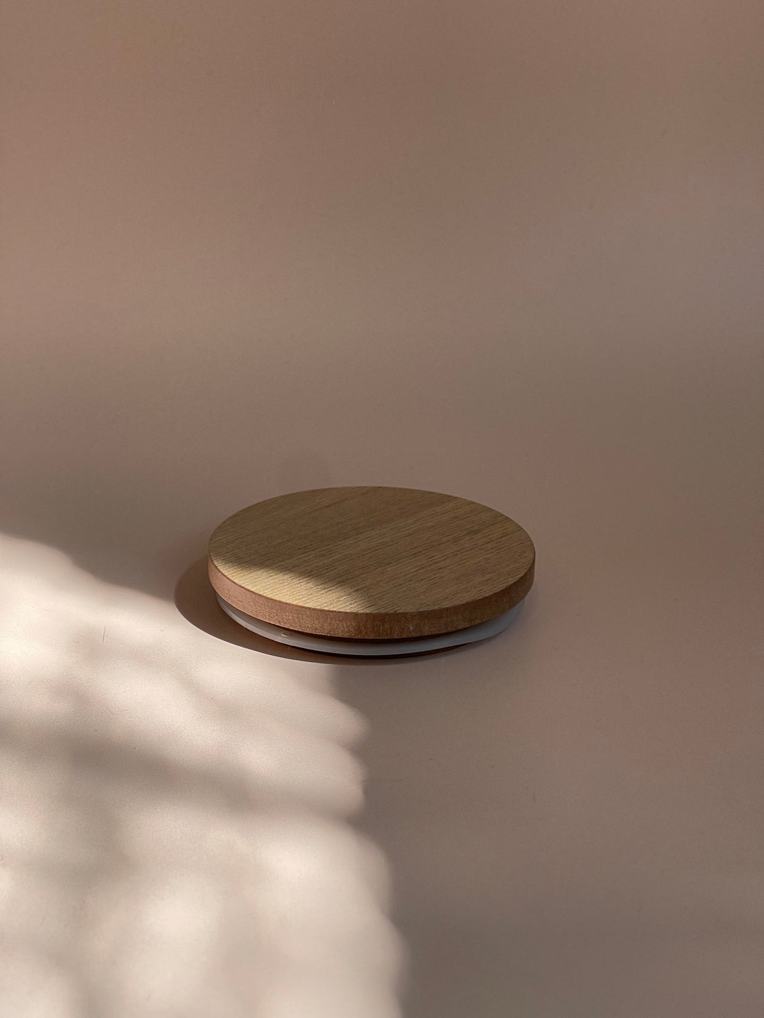 A close-up image of a wooden candle lid, showcasing a natural grain pattern with a smooth finish.